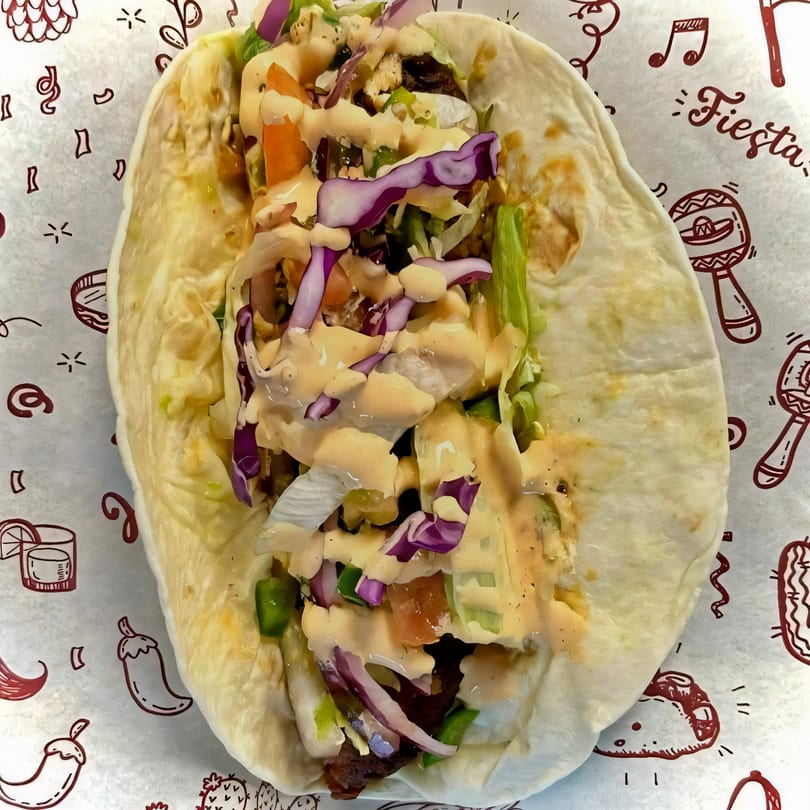 A Fusion Tikka Taco, filled with meat, lettuce, cabbage, and sauce, on a festive paper liner.