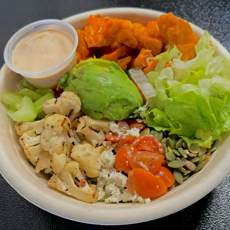 A vibrant Fusion Tikka Taco bowl with chicken, avocado, lettuce, cauliflower, tomatoes, and dressing.