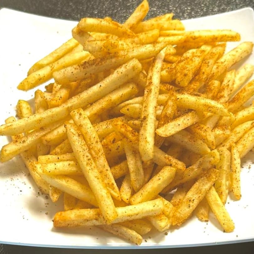 A white plate filled with golden-brown french fries, seasoned with dark spices.